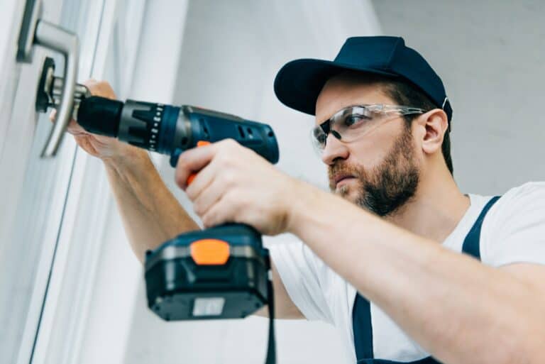 adult repairman in goggles fixing window handle by electric drill